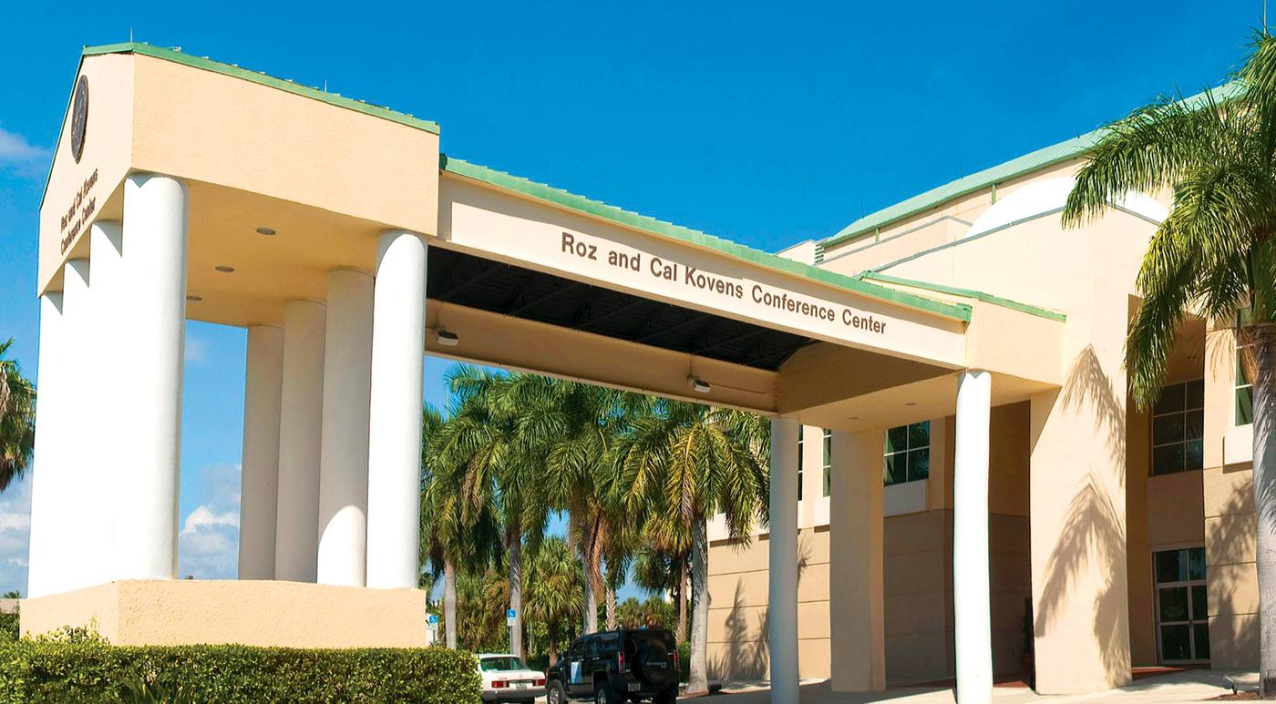 The columned entrance canopy of the Roz and Cal Kovens Conference Center, lined with palm trees under a clear sky.